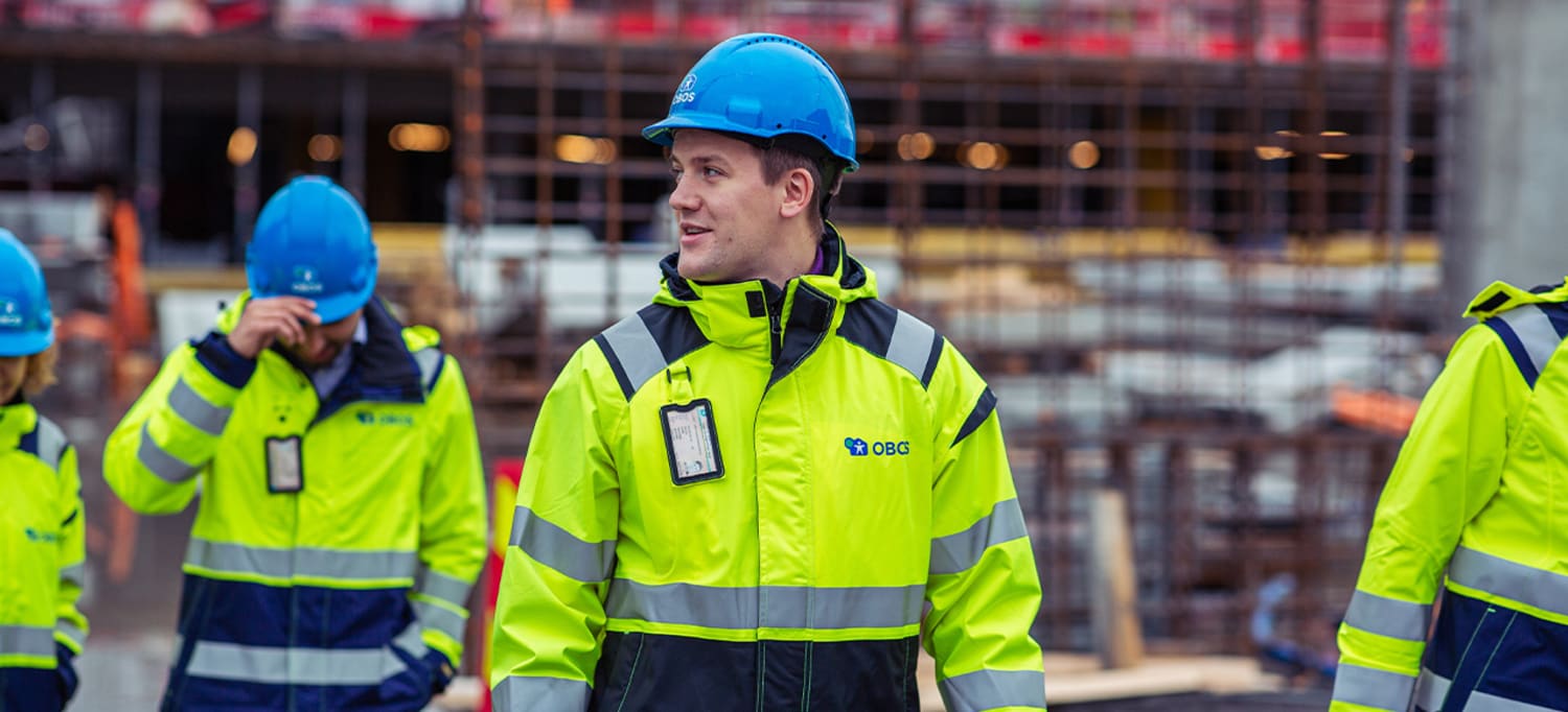 Obos ansatte i uniform og hjelm på befaring på byggeplass.