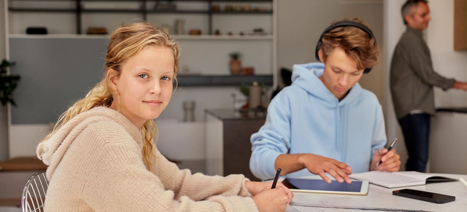 Foto av en ung jente ved spisebordet som ser inn i kameraet, mens en gutt sitter ved siden av.