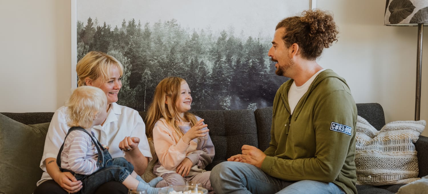Familie på fire smiler og ler i sofa i OBOS Block Watne-bolig