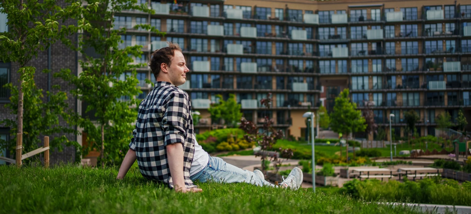 Mann som sitter på gress foran fasaden til et bygg på Ulven