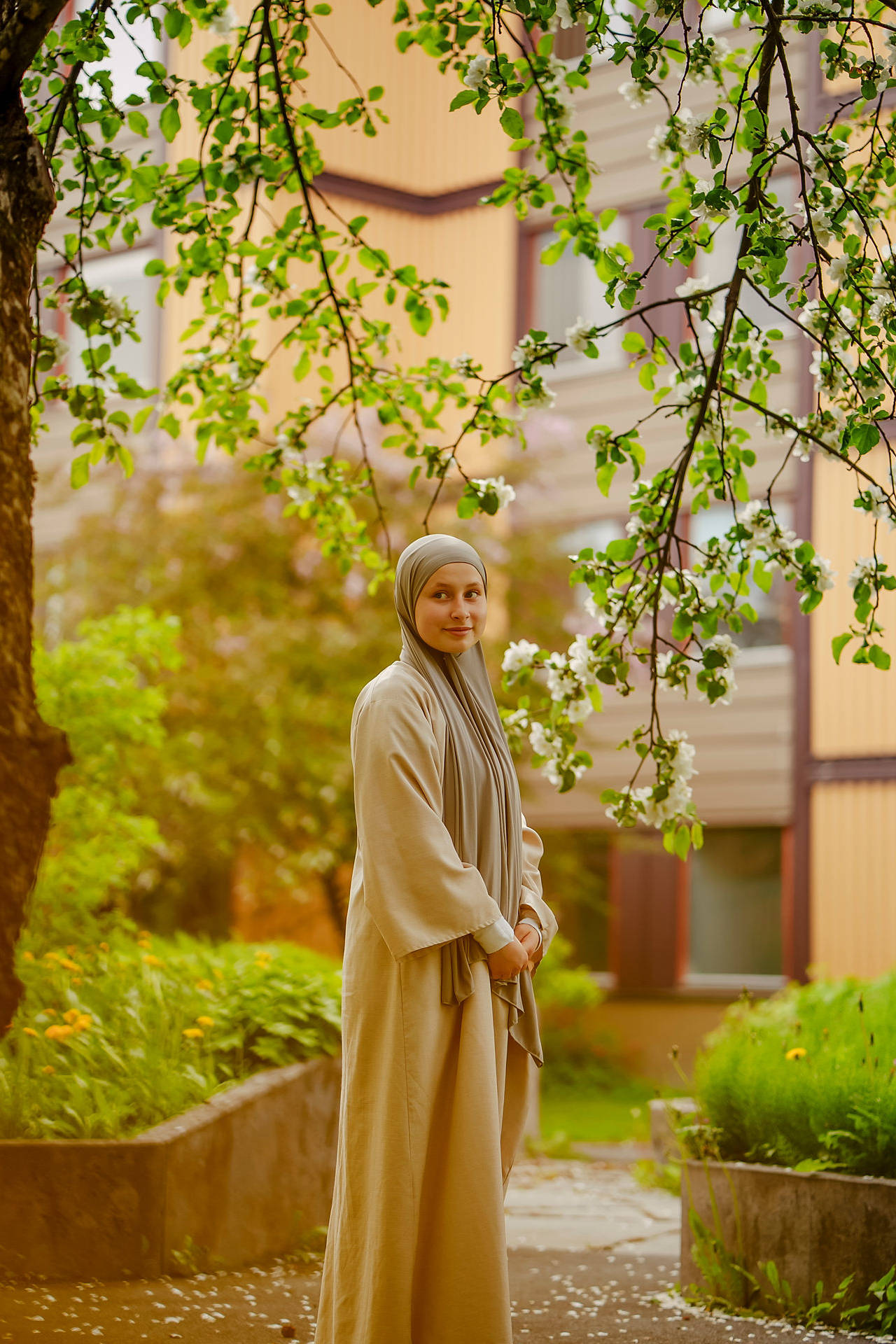 Bilde av Lina Halimi. Hun står under et tre med hvite blomster, og smiler.
