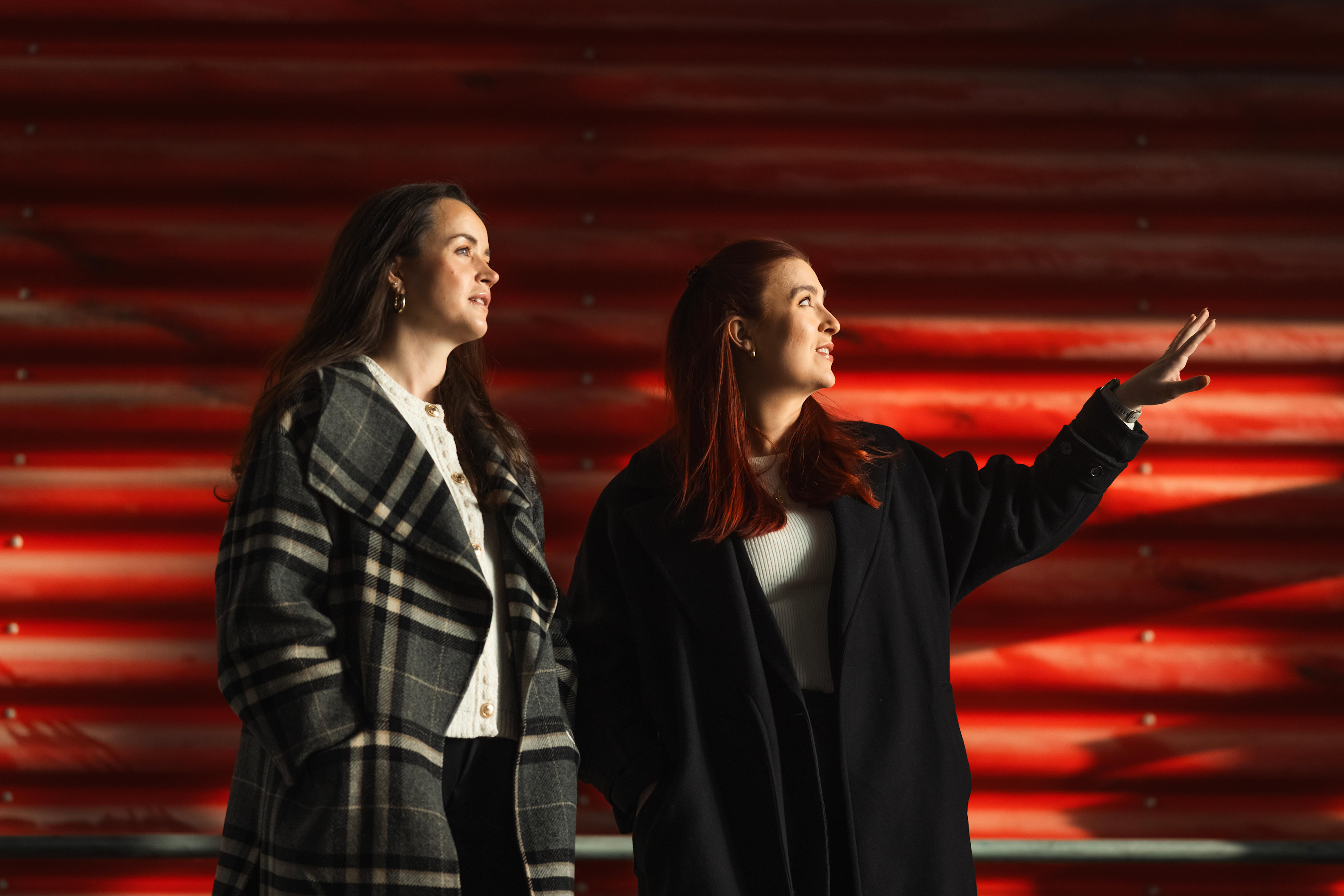 Foto av prosjektleder Karoline Forsnes Krogstad og prosjektselger Mariell Veinan mot rød vegg i de gamle trykkerihallene i Nydalen.