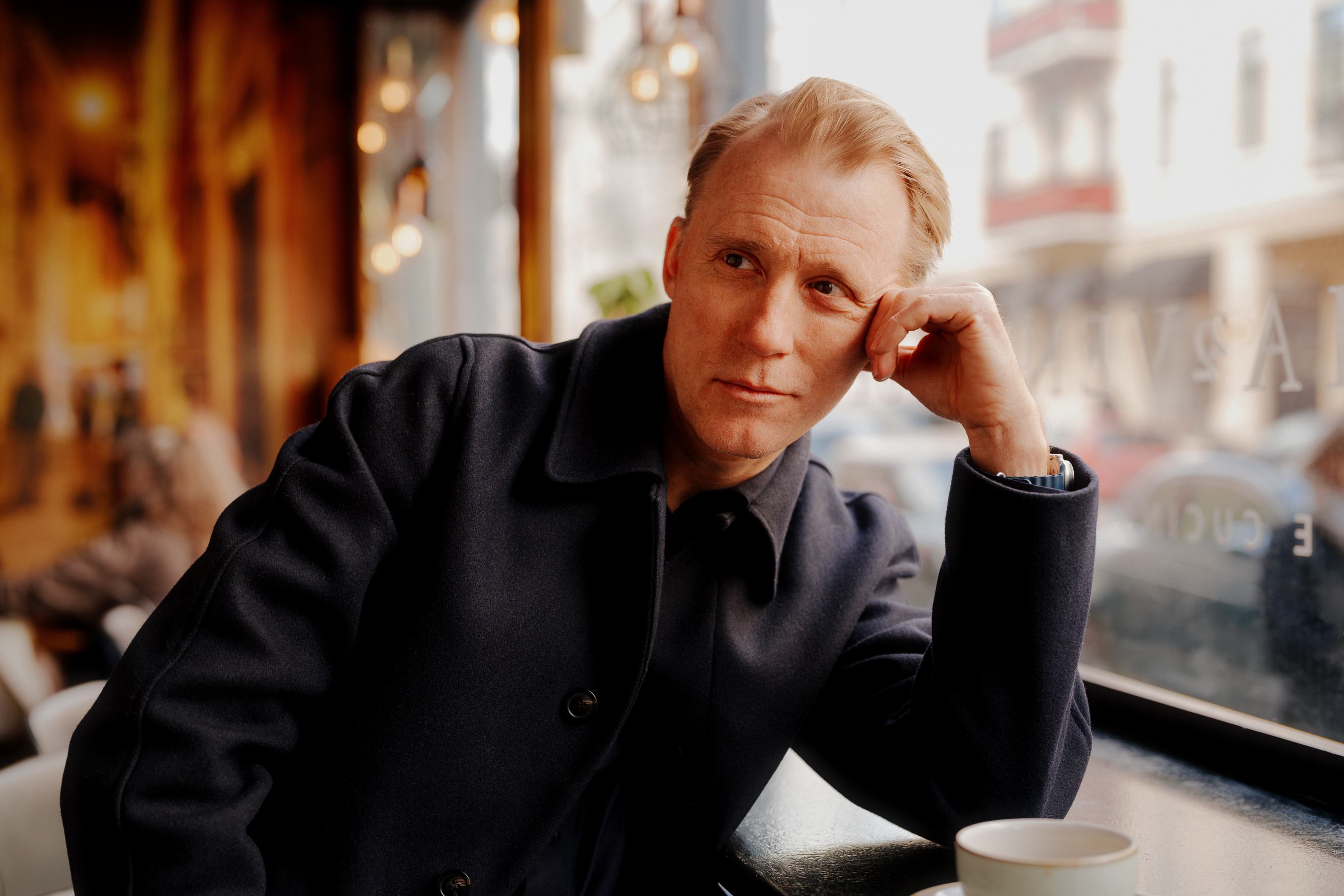 Thorbjørn sitter på en kafé med en kaffekopp. Han har skulderen på bordet og lener ansiktet mot hånden.