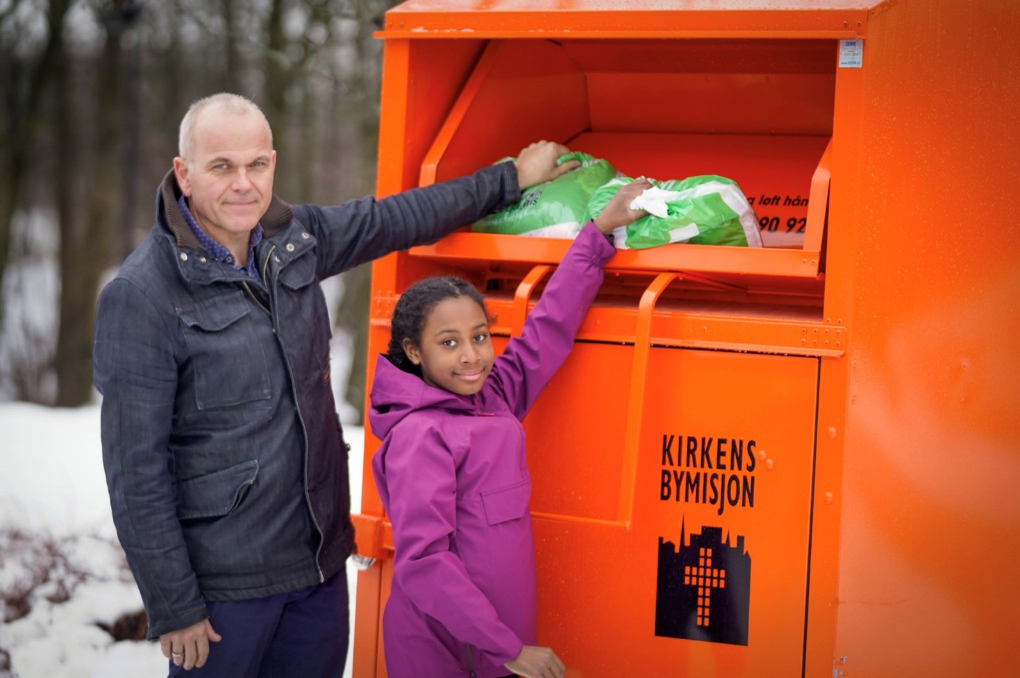 En mann og en jente gir klær i en innsamlingsboks fra Kirkens Bymisjon Foto: Torstein Ihle