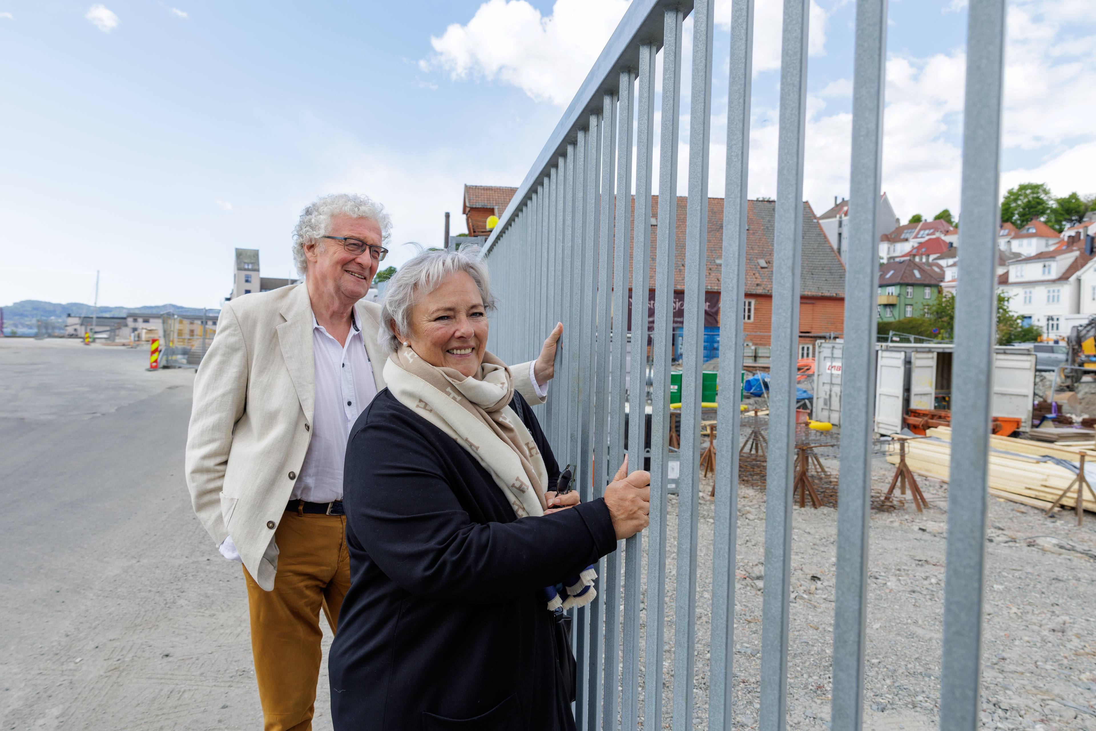 Edna og Øyvind smiler mot kamera mens de holder på et stålgjerde ved byggeplassen til Nøstebukten Brygge