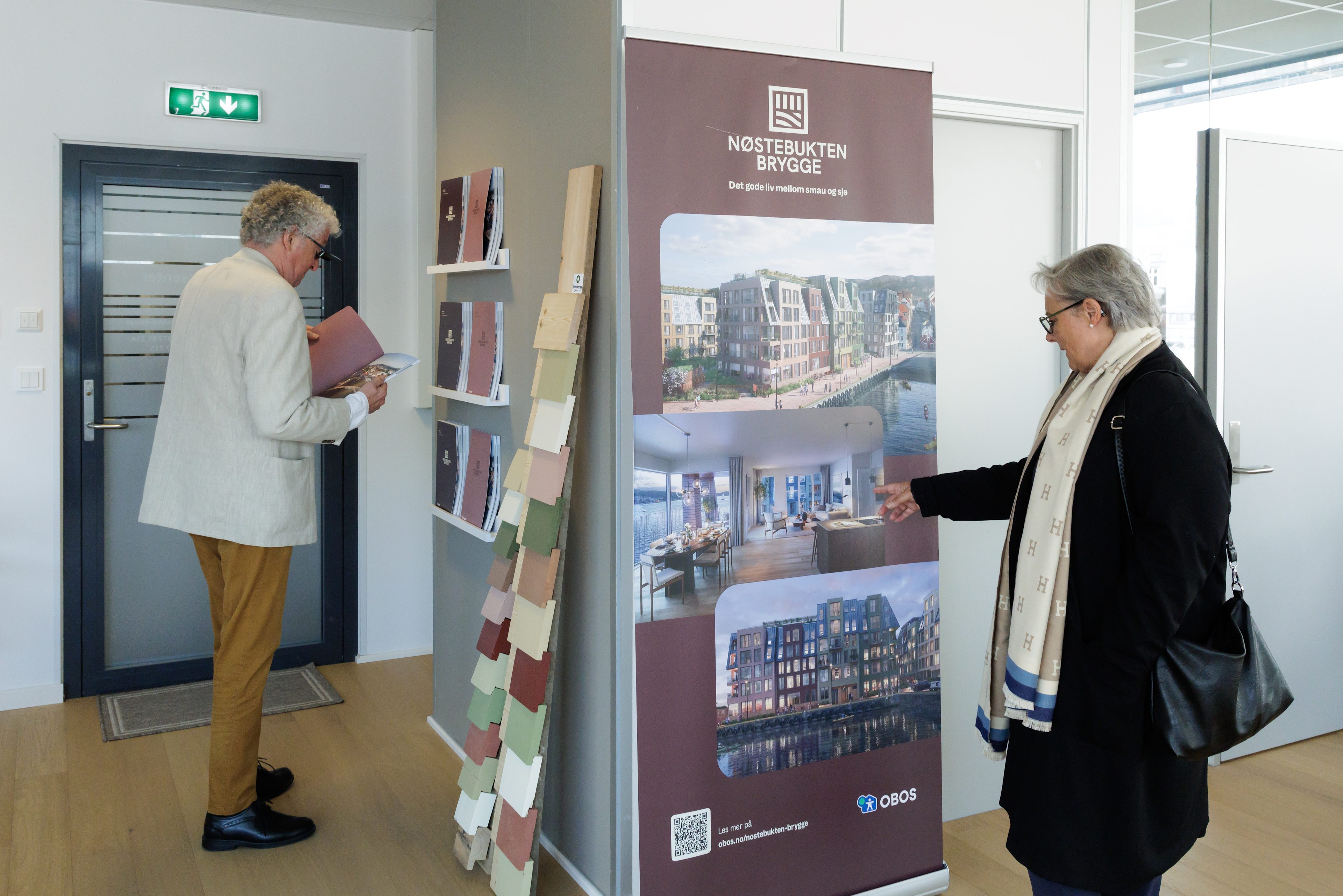 Øyvind og Edna står på visningssenteret til Nøstebukten brygge og lesere kataloger og ser på plakater