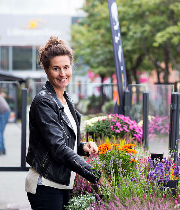 Smilende kvinne arrangerer blomster i blomsterkasse