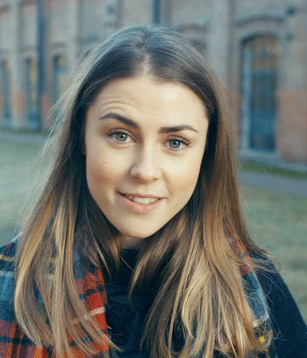 Kvinne med brunt hår ser i kamera og smiler