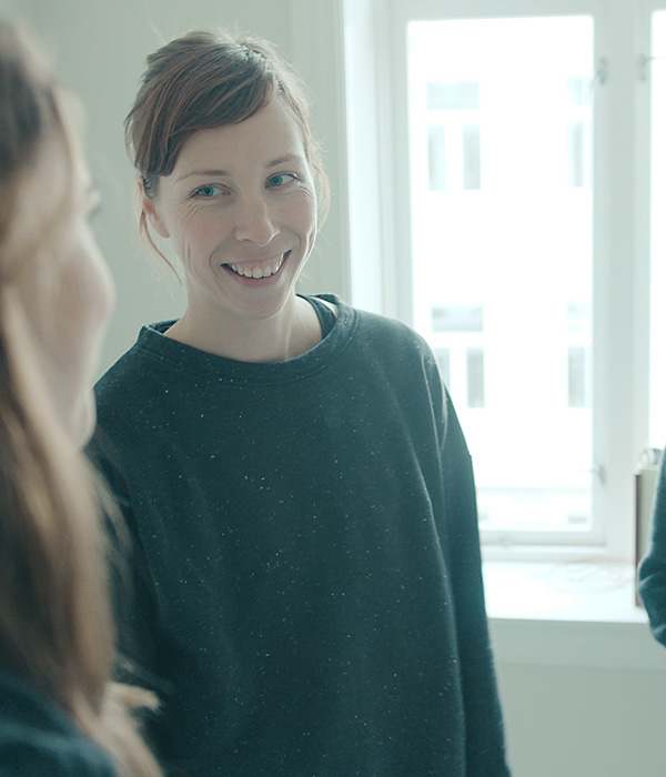 To kvinner og en mann står i en stue og smiler