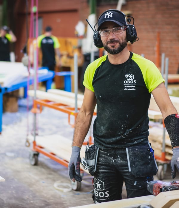 En kille står i arbetarkläder och skyddsglasögon i en OBOS-fabrik