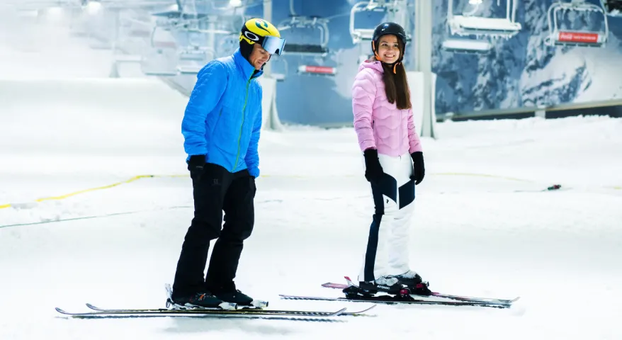 En kvinne og mann står på ski på SNØ. De smiler. 