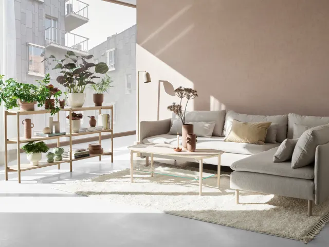 Bilde av en lys stue med en beige sofa og et stort vindu på venstre side som slipper sollys inn i rommet