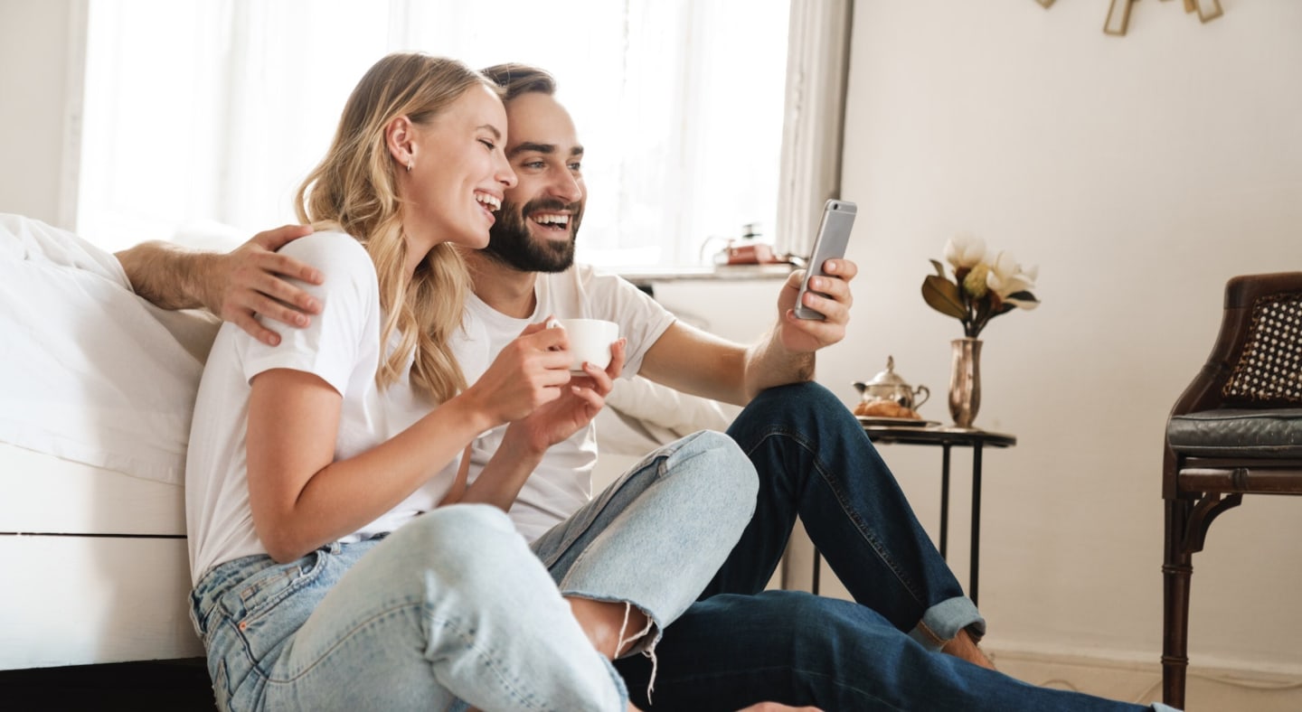 En mann og en dame som sitter å holder rundt hverandre mens de smiler mot en mobiltelefon