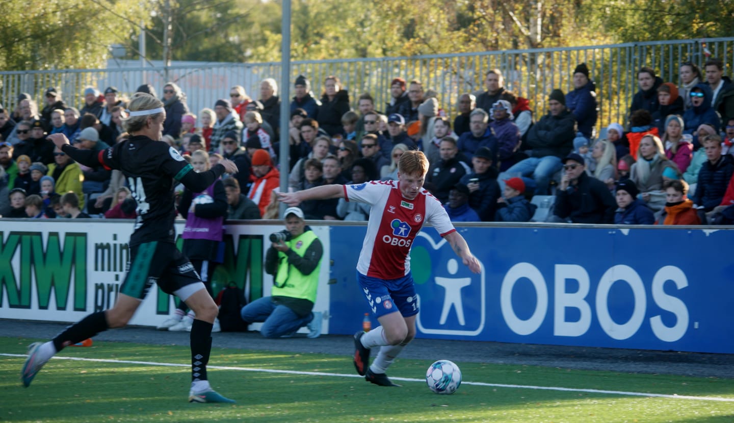 Foto av en KFUM fotballspiller som løper på fotballbanen med ballen foran seg.