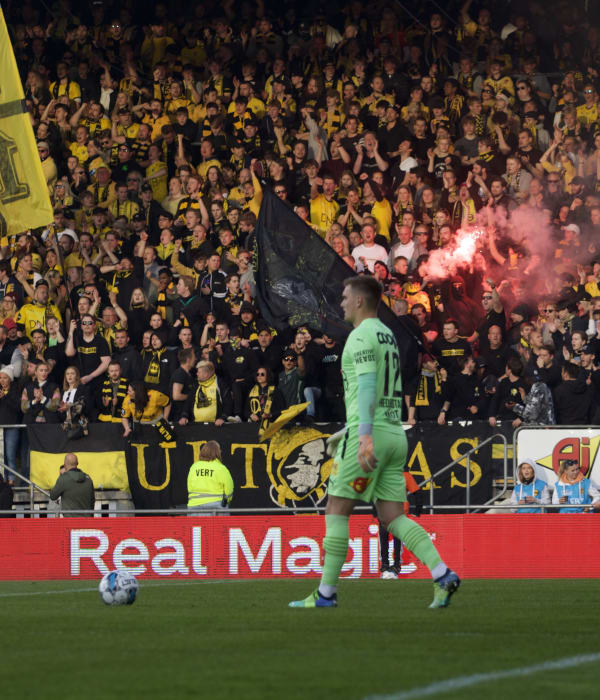 Foto av LSK sin keeper i grønn drakt med LSK supportere som heier fra tribunen i bakgrunnen