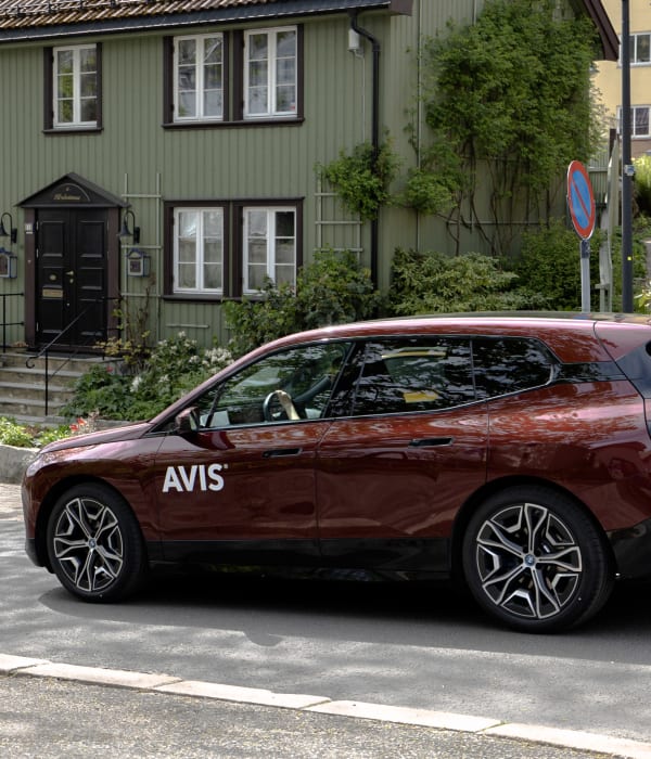 Sommerlandskap i byen og en rød bil på veien.
