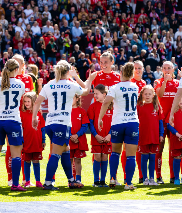 Bilde av to damelag som håndhilser på hverandre ute på en solrik fotballbane.