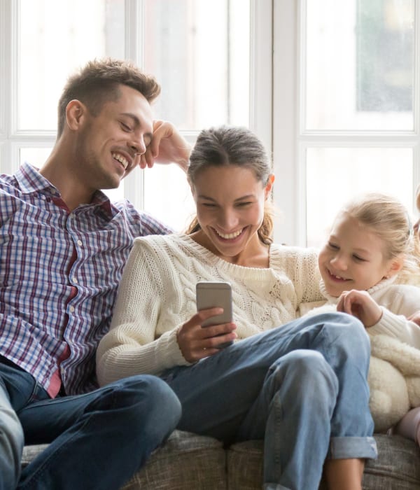 En familie på fire sitter samlet i en sofa, der begge de voksne og barna ser på en telefon o smiler.