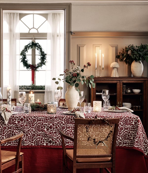 Et julepyntet bord med et juletre i bakgrunnen. Mange fine detaljer på både bordet, i vinduet og på kommoden.