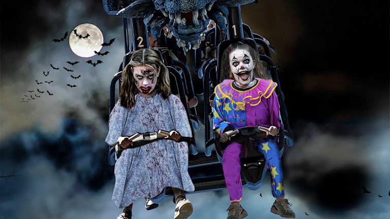 To jenter sitter i en karusell og har kledd seg ut. Det er Halloween og ser skummelt ut.