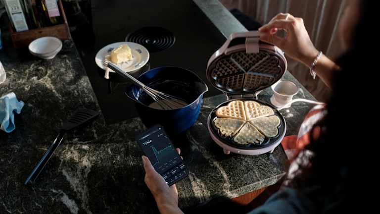 En person steker vafler og ser samtidig i en app hvor mye strømmen koster.