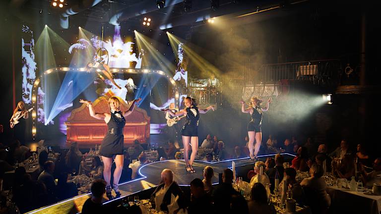 Tre damer står på en scene og danser. 