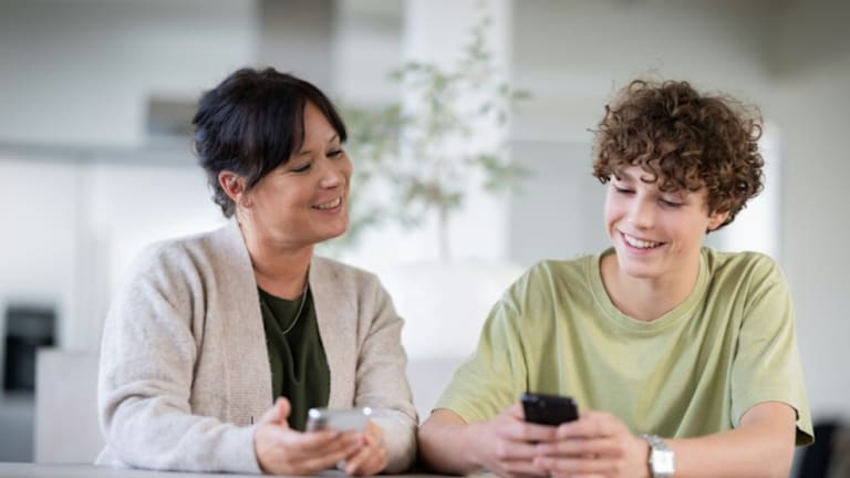 En mann sitter med en grønn skjorte og taster på mobilen, han smiler.