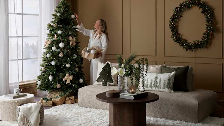 Bilde av en lys stue med en beige sofa og et stort vindu på venstre side som slipper sollys inn i rommet