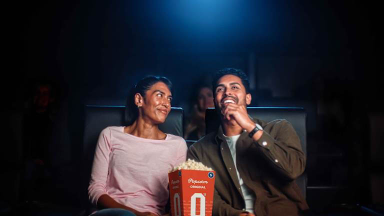 Tre barn sitter i en kinosal og ser på en film. De smiler. Hun ene jenta har popcorn og en annen jente har brus.