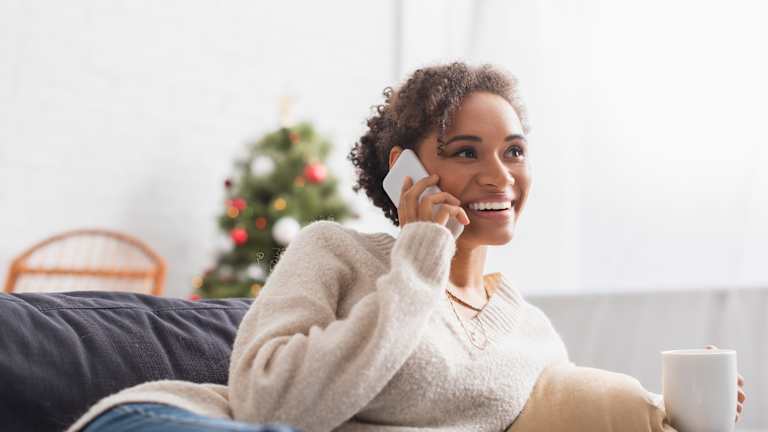 En dame snakker i mobiltelefonen. Hun smiler. Bak henne står et juletre.