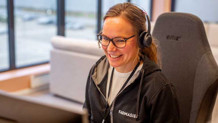 En dame fra kundeservice hos Farmasiet snakker i telefonen og smiler.