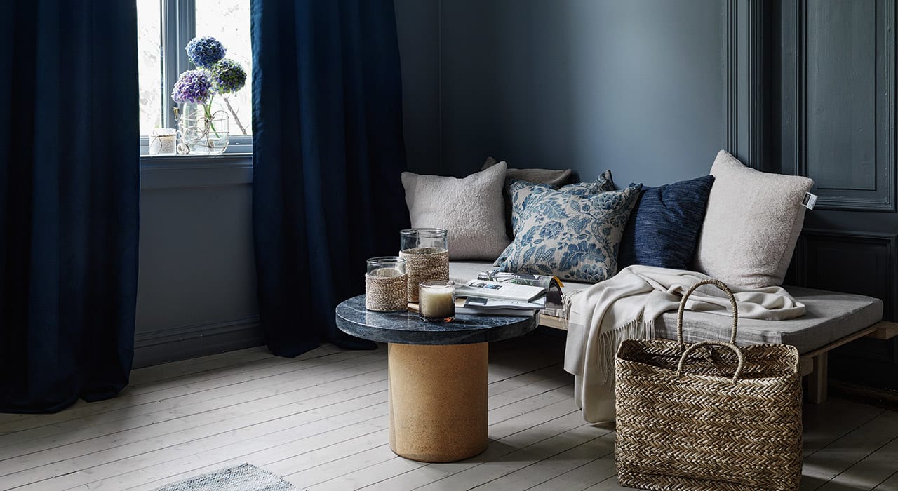 Stue med blå velurgardiner, sofa og sofabord, lyst tregulv og mørkeblå vegger