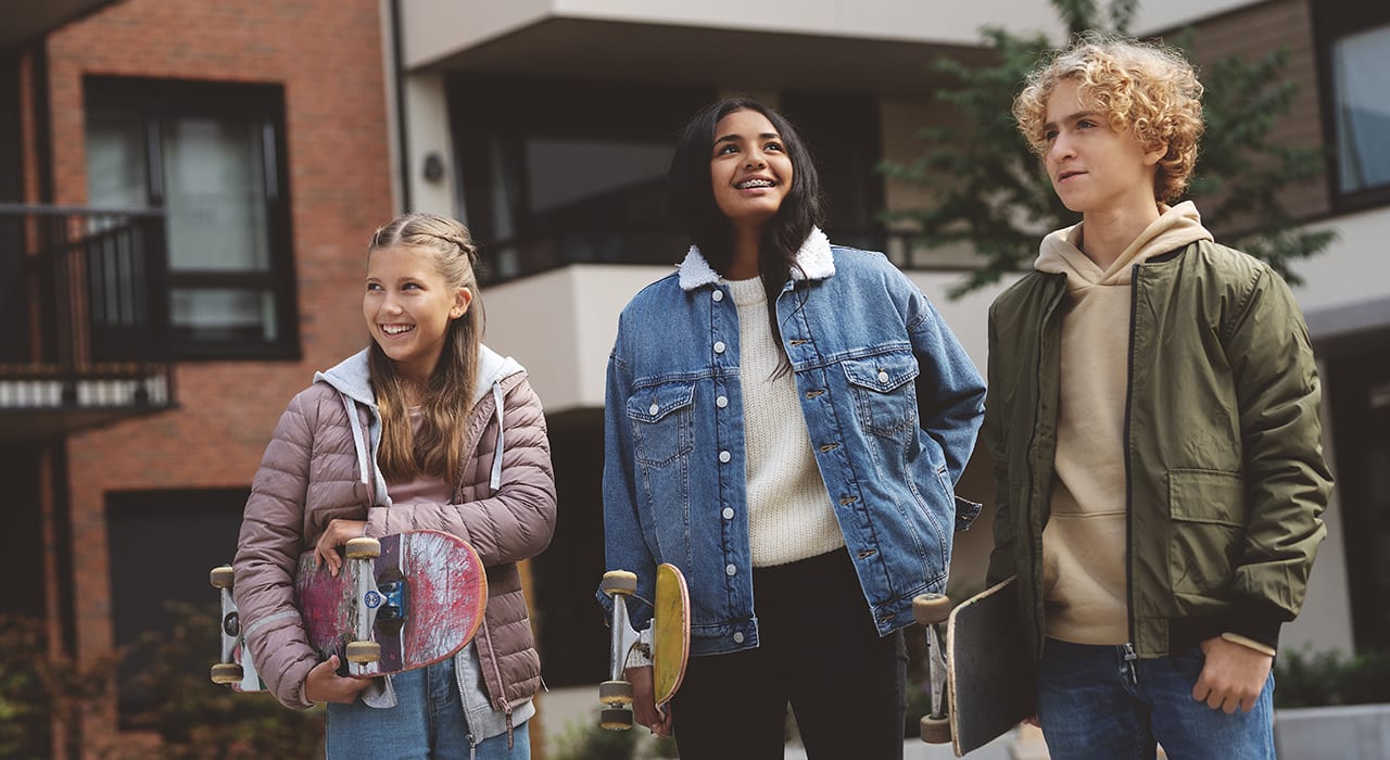 Tre ungdommer som smiler med skateboard under armene.