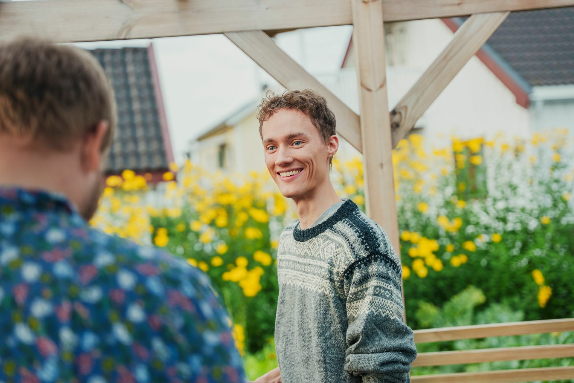 Sigurd har på seg en ullgenser og står å smiler til en av naboene i kvarteret