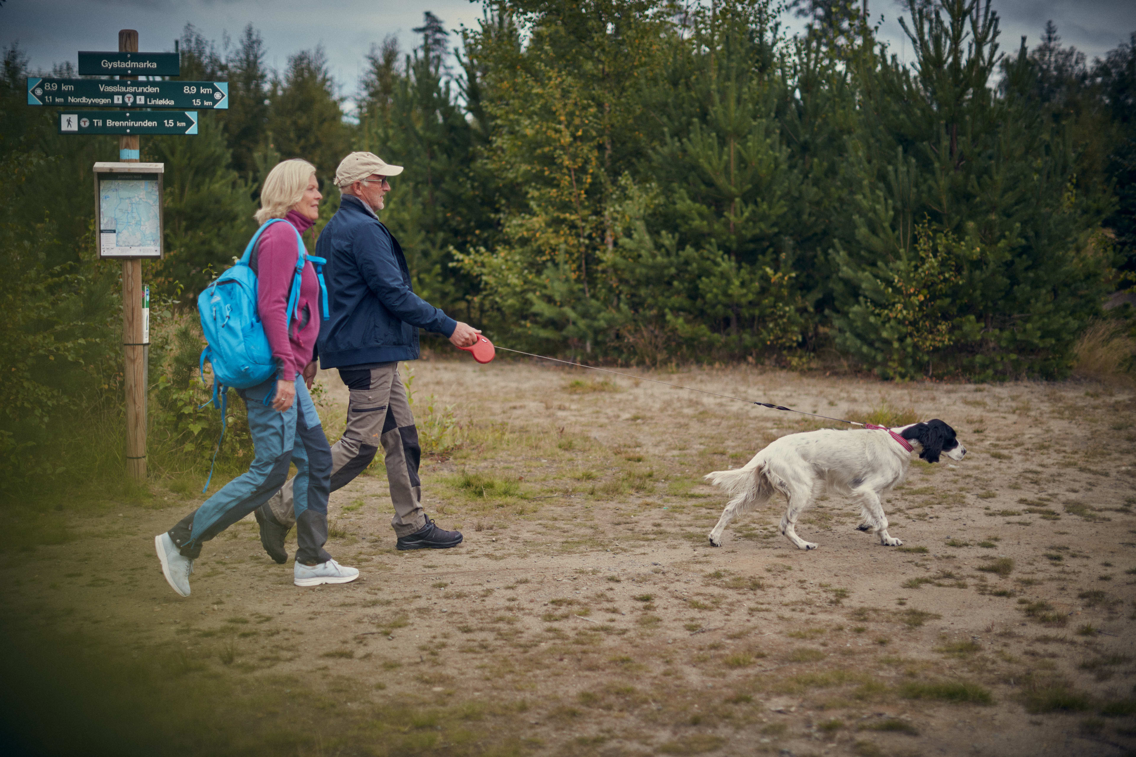 Foto av et par som går tur med en hund i skogen på Jessheim.