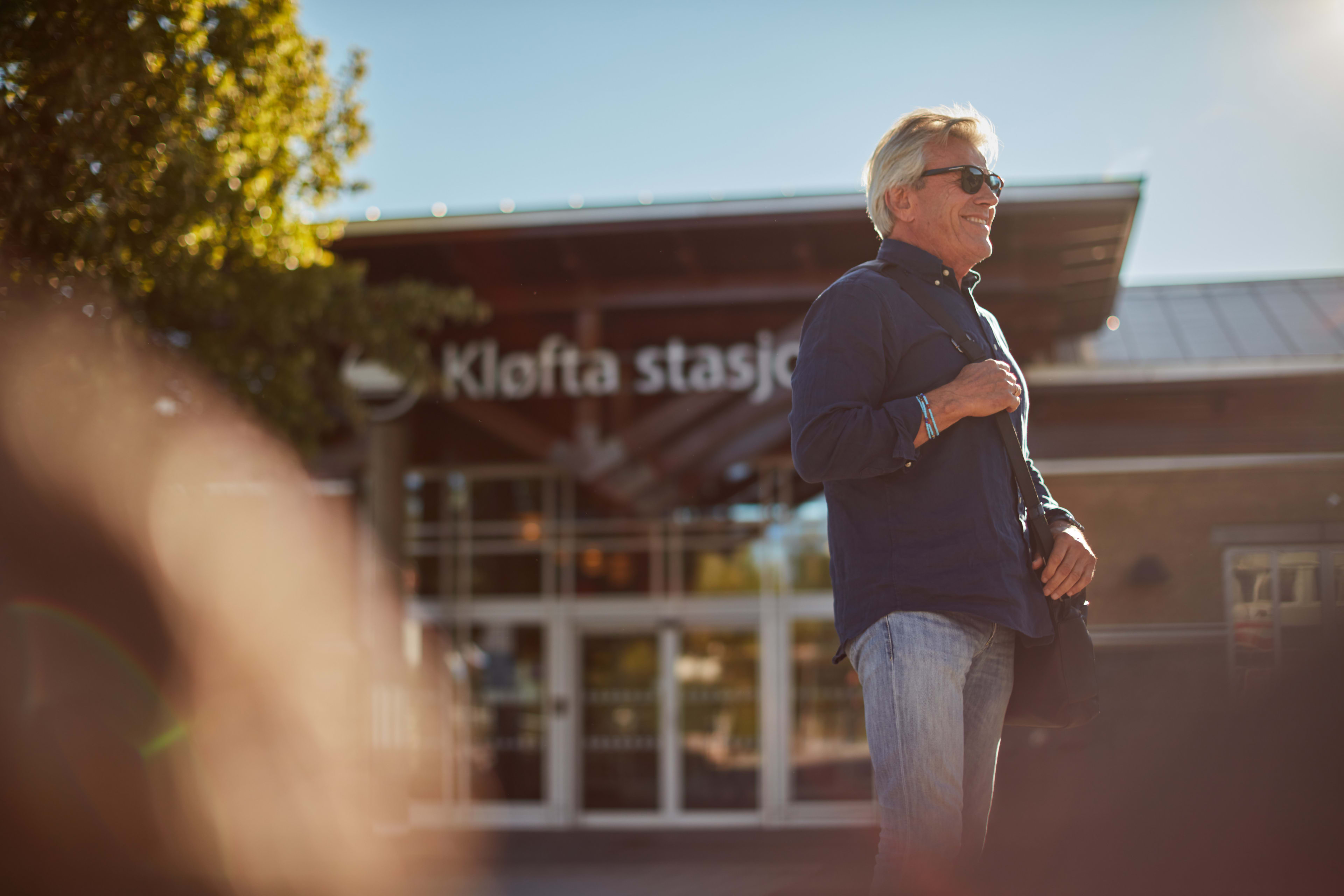 Mann som står foran inngangen til Kløfta stasjon på sommeren.