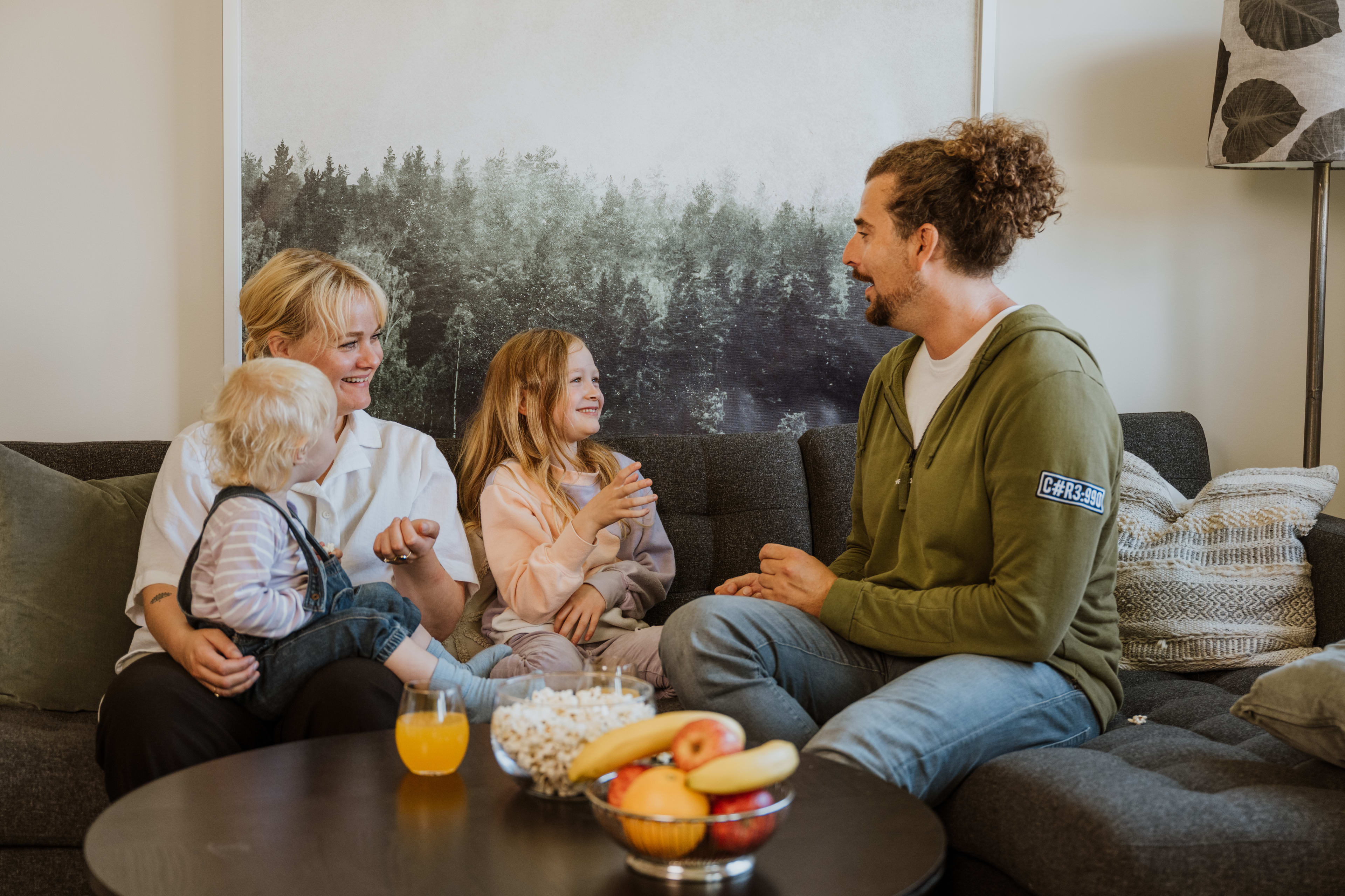 Familie på fire smiler og ler i sofa i OBOS Block Watne-bolig