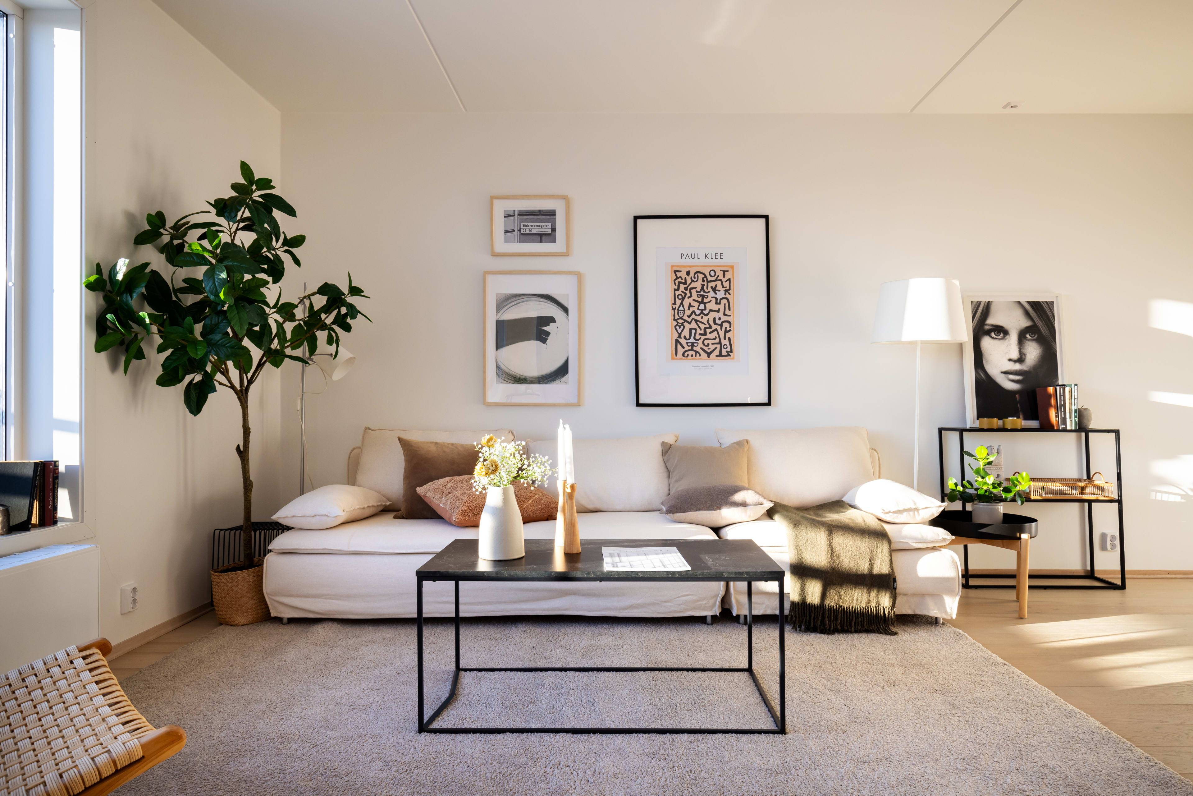 Hvitmalt stue med hvit sofa, stuebord og en bildevegg i en leilighet i Løren botaniske