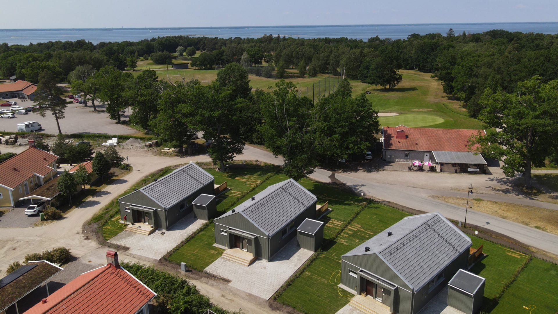 Drönarbild: Tre enplanshus med altan. I bakgrunden skog, golfbana och vatten.