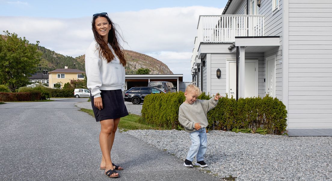 Smilende mor og sønn står foran et hvit hus