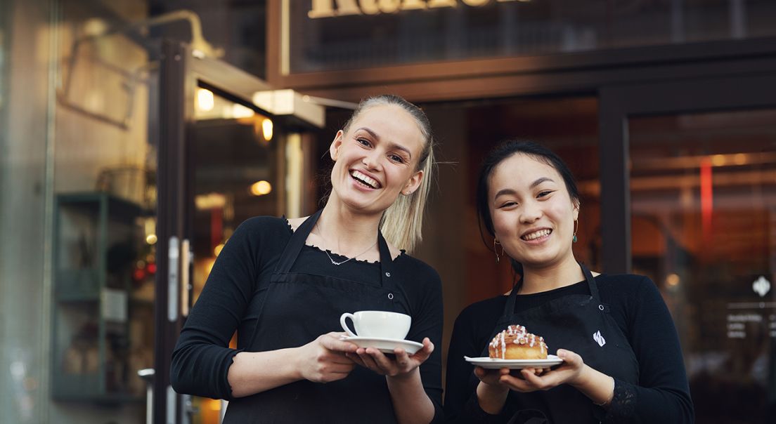 To baristaer står utenfor Kaffebrenneriet med kaffe og bakverk