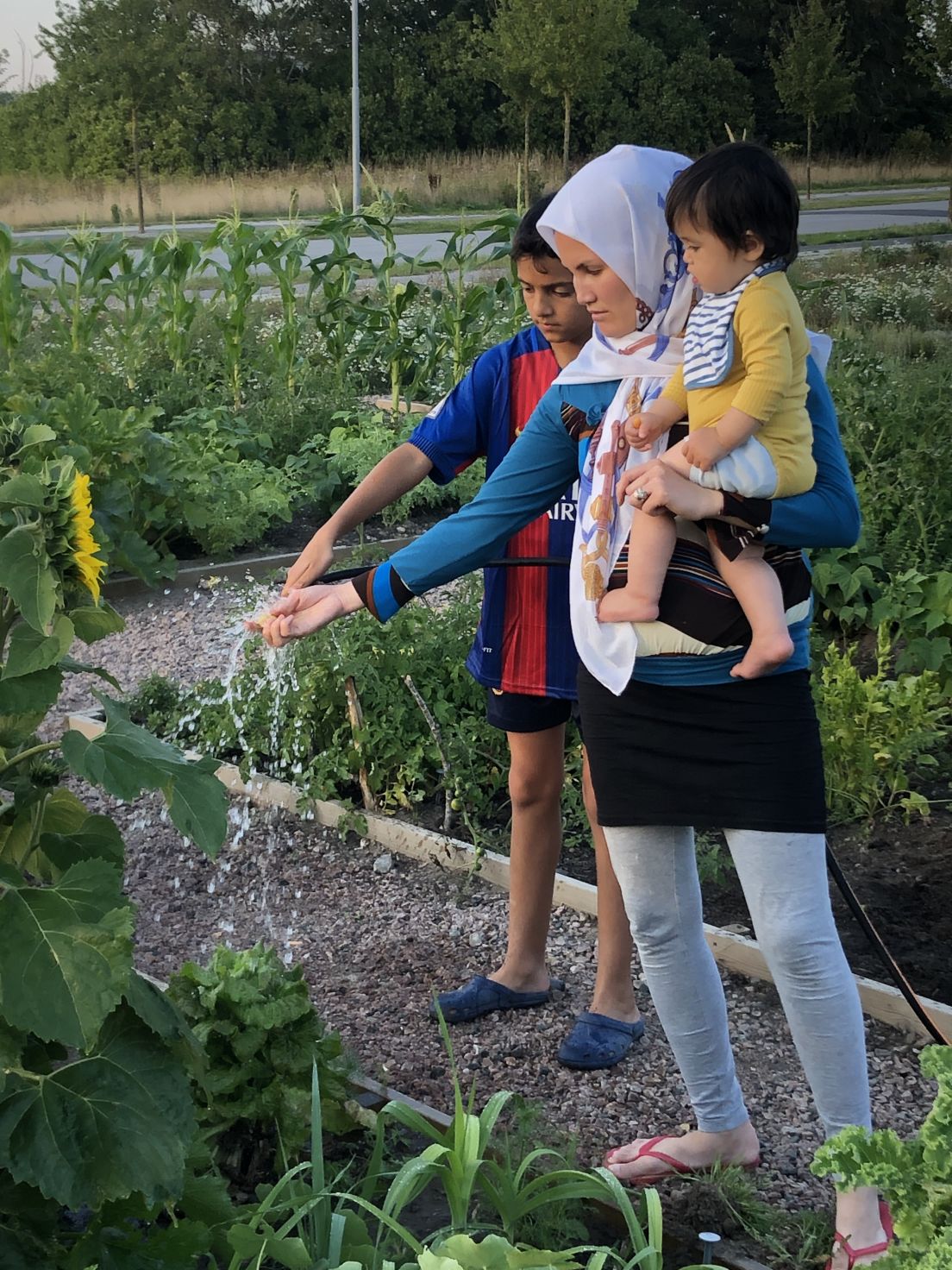 En mamma med ett barn i famnen och ett bredvid vattnar sina grödor