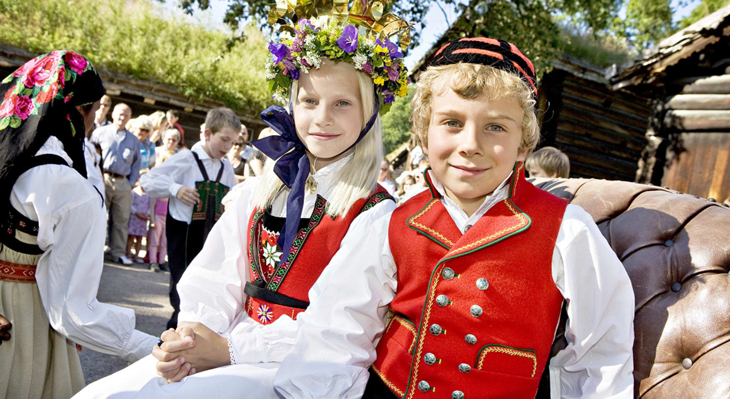 En bunadskledd gutt og jente sitter i en kjerre.
