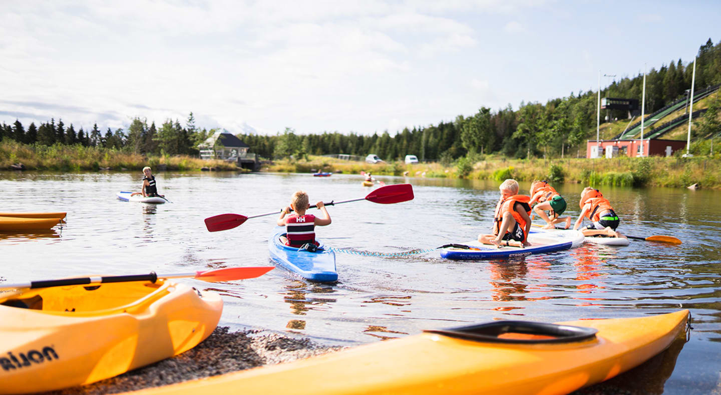 Barn i kajak og standup-paddling-brett på en sjø