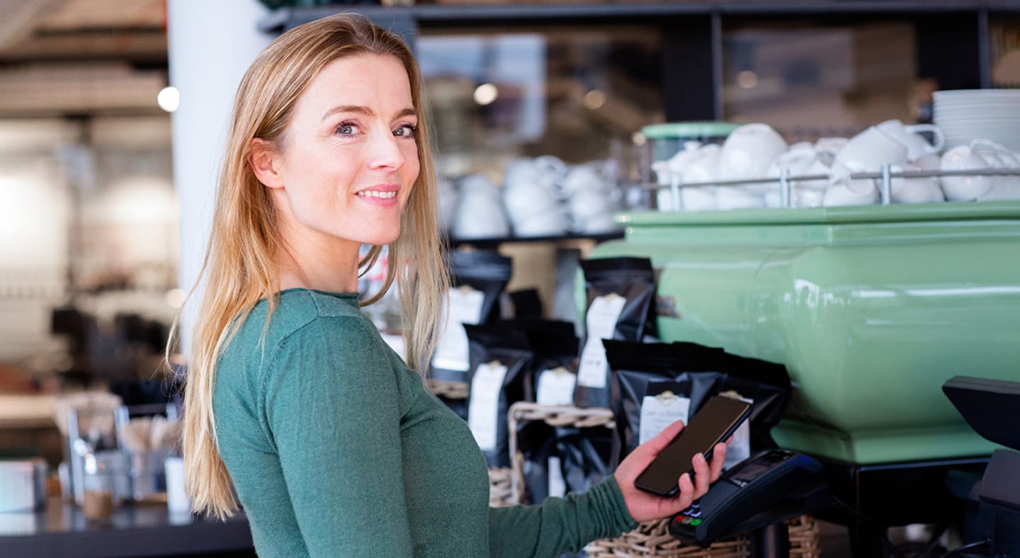 Dame i en kaffebar som betaler med bankkort på mobilen.