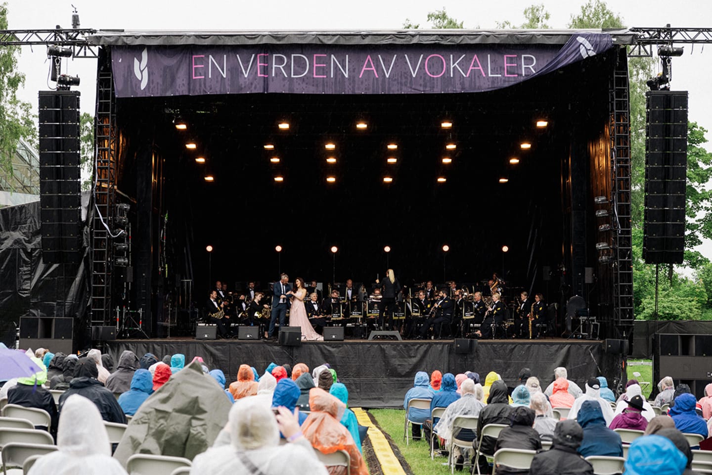 Bilde av en stor, utvendig scene med et orkester og to sangere, Publikum sitter og ser mot scenen.