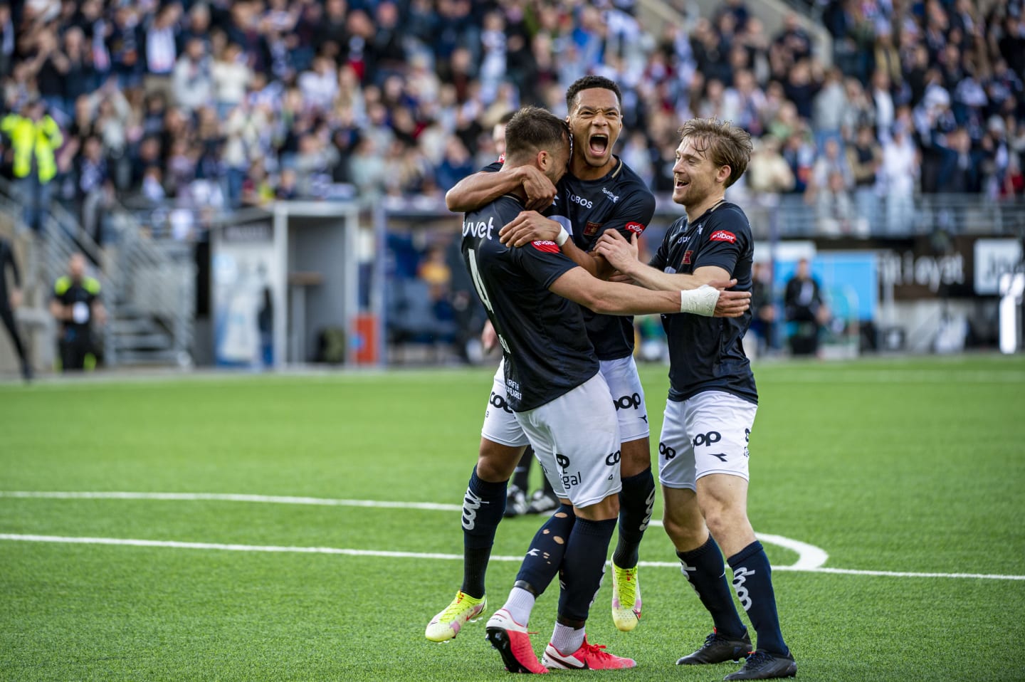 Tre fotballspillere fra Viking som klemmer og feirer sammen på den grønne fotballbanen