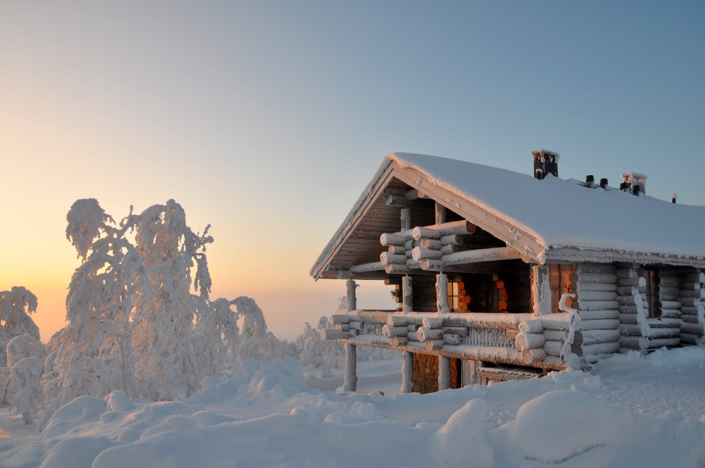 En gammel trehytte i skogen som er dekket med snø på både tak og vegger.