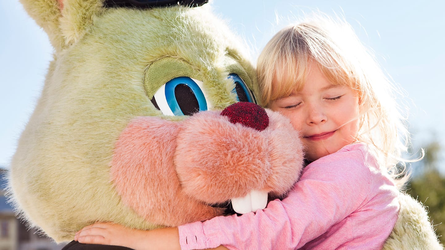 Liten jente som klemmer Liseberg maskoten i sommerdag.