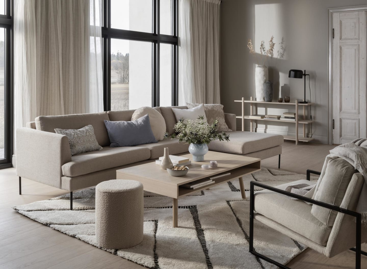 Foto av en møblert stue med en beige sofa, lyst trebord og en store vinduer.